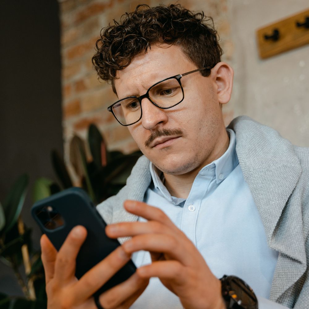 Pessoa de óculos lendo atentamente as informações na tela do celular.